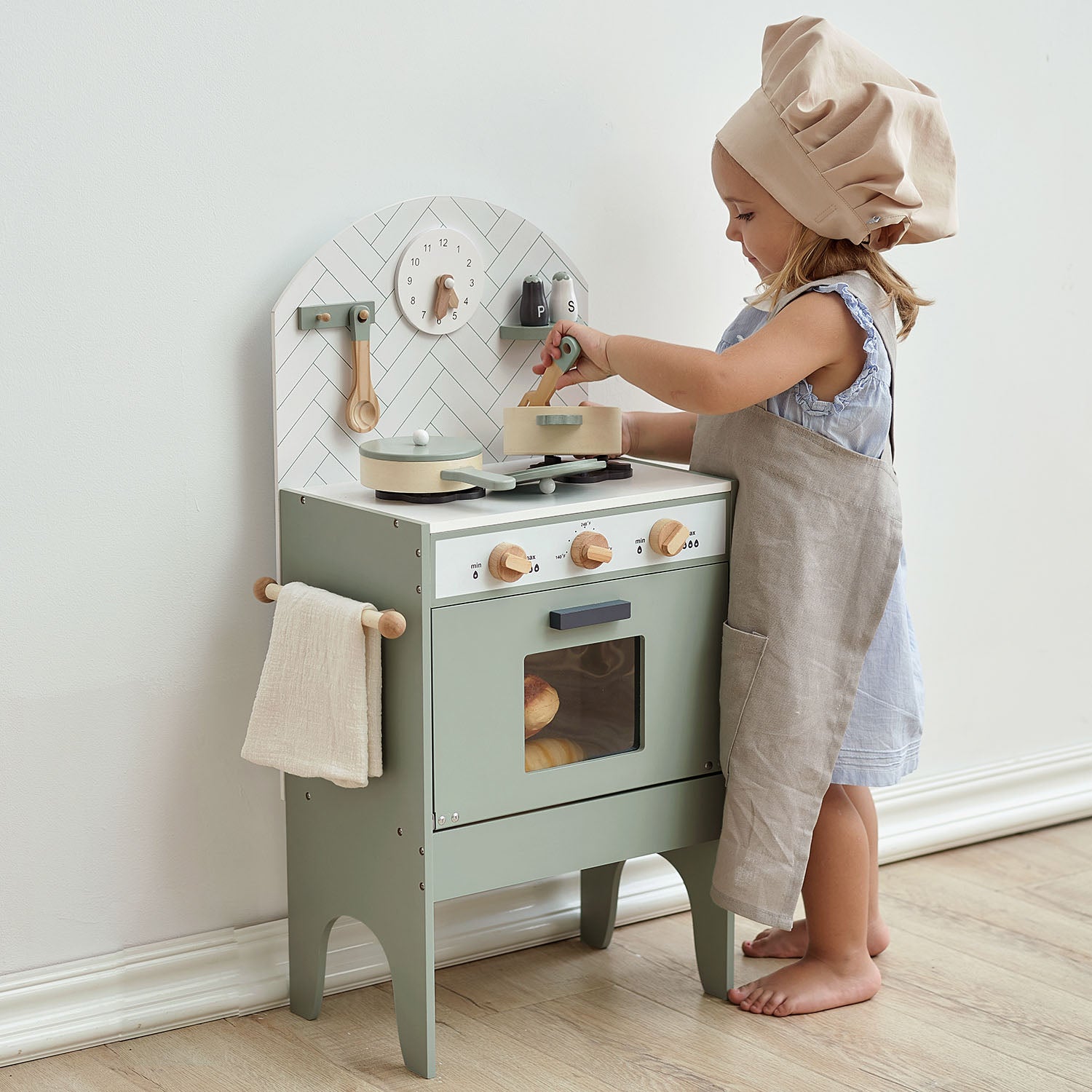 Child playing with a toy kitchen set in a room with a white wall.