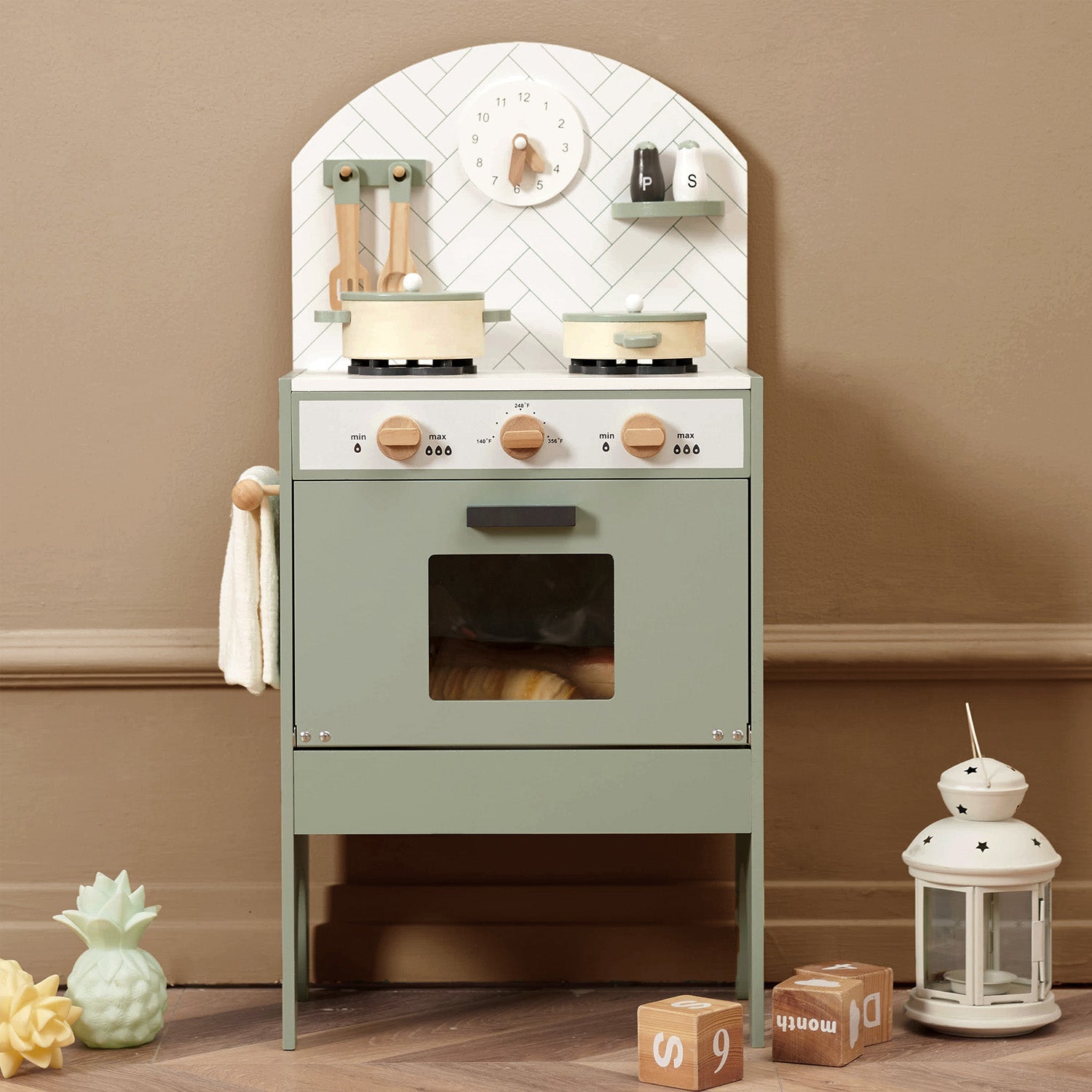 Children's play kitchen set against a beige wall with decorative items on a wooden floor.